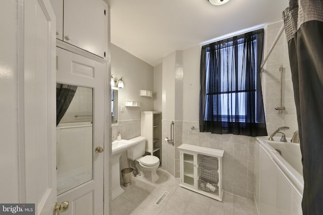 bathroom with toilet, tile walls, wainscoting, tile patterned floors, and a bathtub