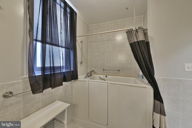 bathroom with a shower with shower curtain, a garden tub, and tile walls