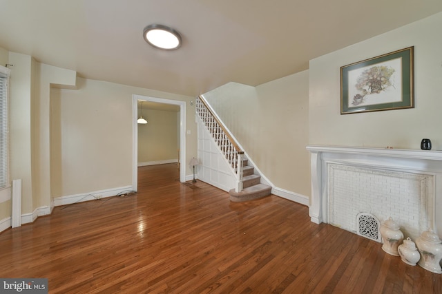 unfurnished living room featuring baseboards, stairway, and wood finished floors