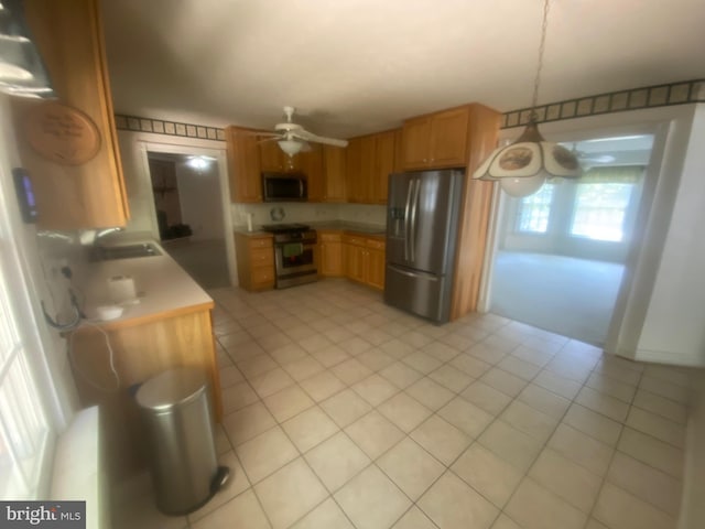 kitchen with brown cabinetry, ceiling fan, appliances with stainless steel finishes, light countertops, and a sink