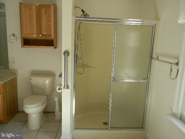 full bath with toilet, a shower stall, vanity, and tile patterned floors