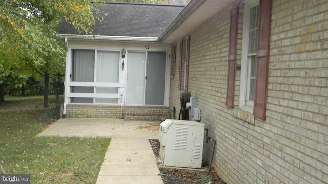 view of exterior entry featuring a shingled roof, a patio, and brick siding