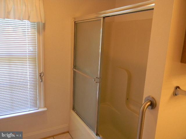 full bathroom featuring tile patterned flooring, baseboards, and bath / shower combo with glass door