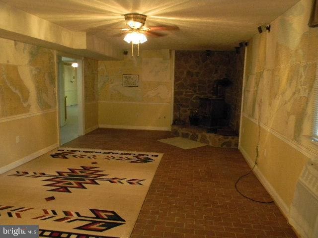 basement featuring a fireplace, a wood stove, and ceiling fan