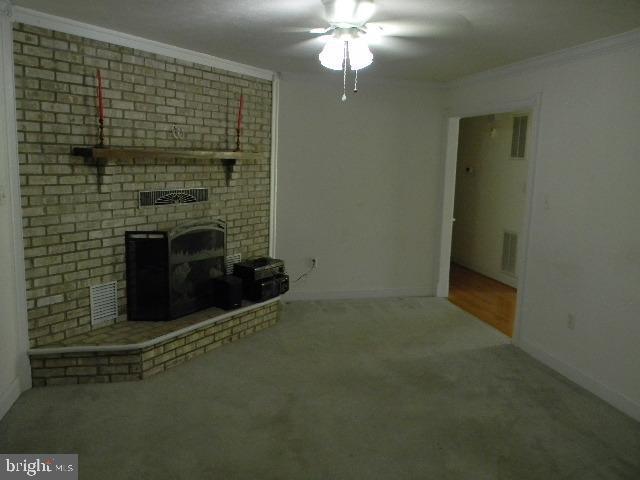 unfurnished living room with carpet flooring, a ceiling fan, baseboards, ornamental molding, and a brick fireplace