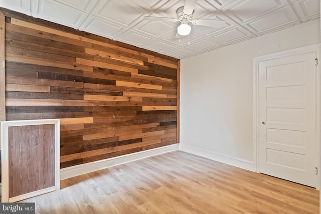 spare room featuring wooden walls, light wood-type flooring, and ceiling fan