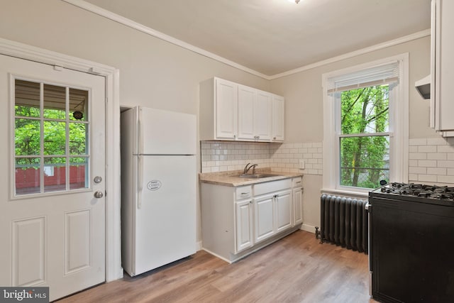 kitchen featuring decorative backsplash, radiator, sink, white refrigerator, and white cabinetry