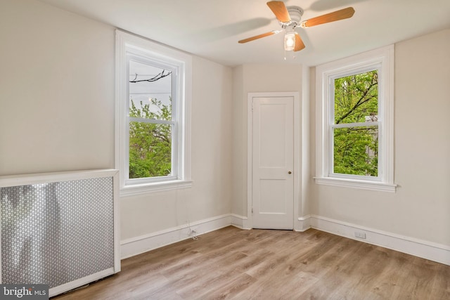 unfurnished room featuring ceiling fan, radiator heating unit, and light wood-type flooring