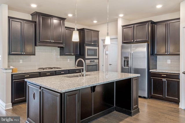 kitchen with sink, an island with sink, decorative light fixtures, wood-type flooring, and stainless steel appliances