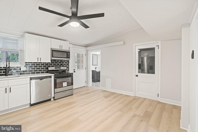 kitchen featuring appliances with stainless steel finishes, vaulted ceiling, sink, white cabinetry, and light hardwood / wood-style floors