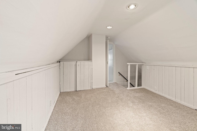 additional living space featuring wood walls, vaulted ceiling, and light carpet