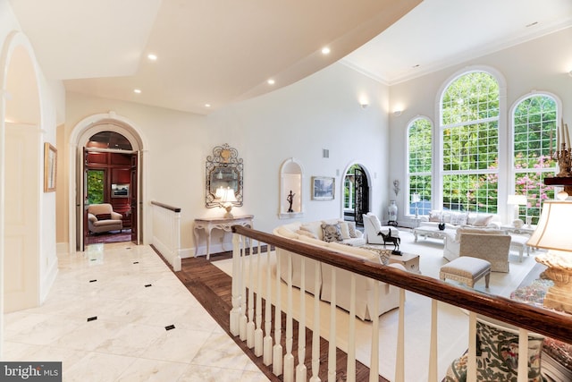 hallway featuring light hardwood / wood-style floors, ornamental molding, and a towering ceiling