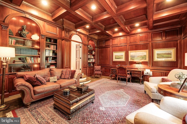 living room with beamed ceiling, built in shelves, coffered ceiling, wooden walls, and crown molding