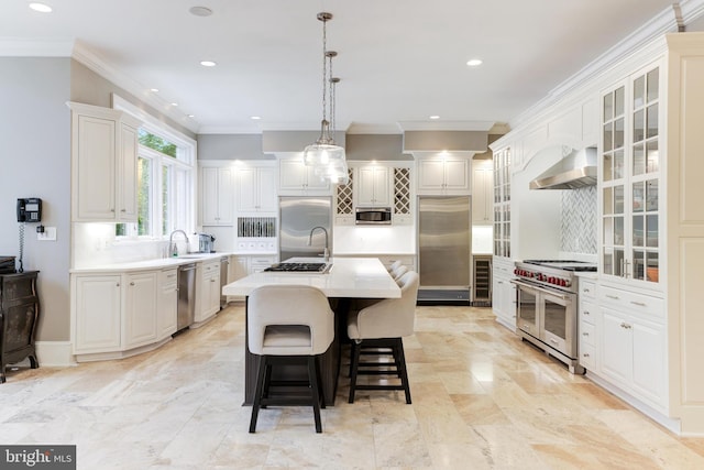 kitchen with an island with sink, white cabinetry, wall chimney range hood, ornamental molding, and high quality appliances