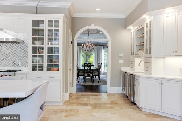 kitchen featuring white cabinets, backsplash, light hardwood / wood-style flooring, ornamental molding, and wall chimney range hood