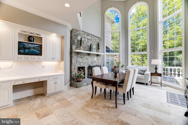 dining room featuring crown molding, a stone fireplace, and a towering ceiling