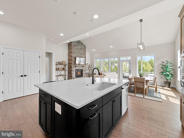 kitchen with vaulted ceiling, a fireplace, a center island with sink, light hardwood / wood-style floors, and sink