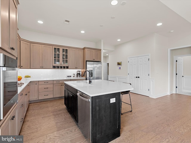 kitchen featuring light hardwood / wood-style flooring, appliances with stainless steel finishes, sink, a center island with sink, and tasteful backsplash