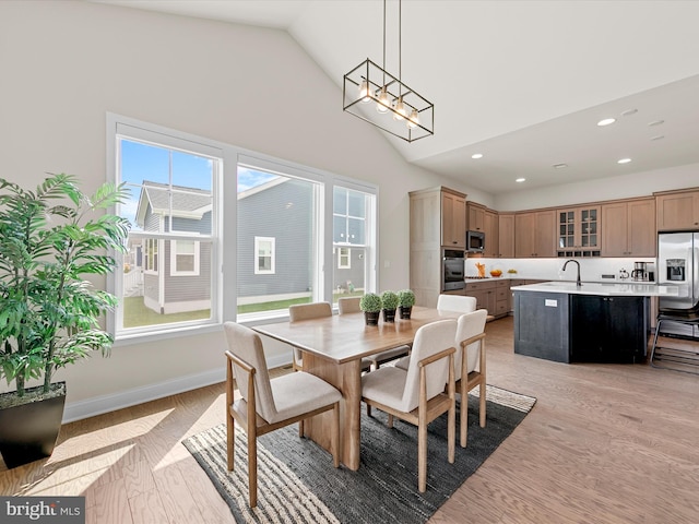 dining space featuring light wood-type flooring, high vaulted ceiling, and sink