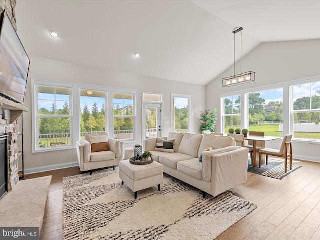 living room featuring light hardwood / wood-style flooring, a stone fireplace, and high vaulted ceiling