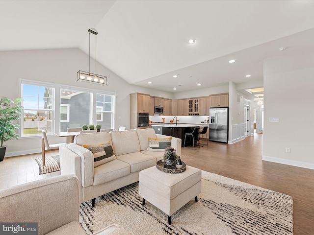 living room with light wood-type flooring, high vaulted ceiling, and sink