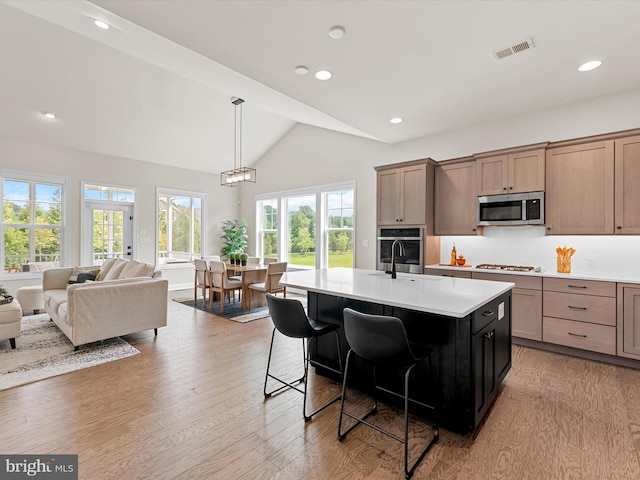 kitchen with a kitchen breakfast bar, a kitchen island with sink, stainless steel appliances, decorative backsplash, and light wood-type flooring