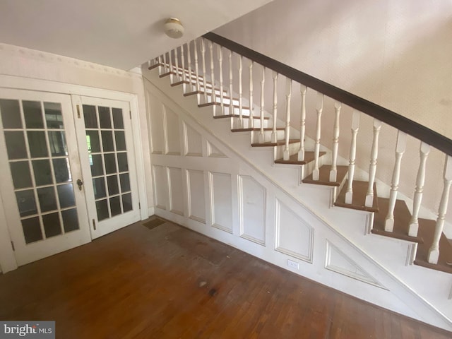 stairway featuring french doors, a decorative wall, and wood finished floors