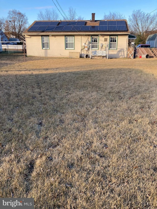 rear view of property with a lawn and solar panels