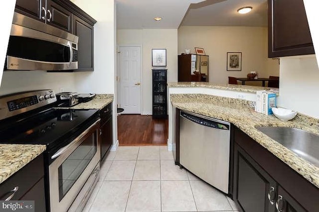 kitchen with stainless steel appliances, light stone countertops, dark brown cabinetry, and light tile patterned flooring