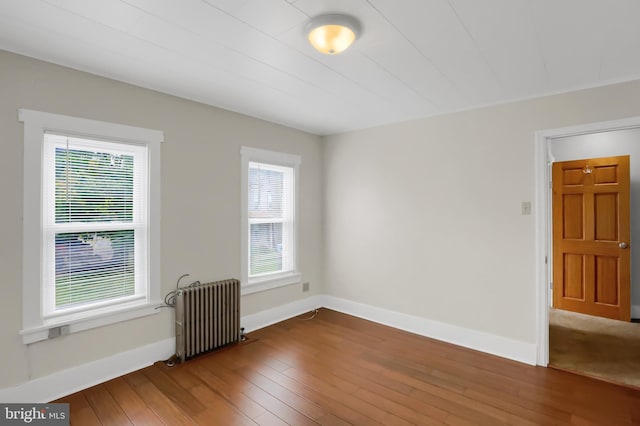 unfurnished room featuring radiator heating unit, a wealth of natural light, and hardwood / wood-style flooring