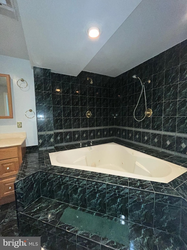 bathroom with a combined bath / shower with jetted tub, tile walls, and vanity