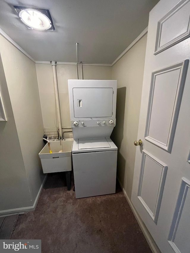 laundry area with stacked washer and clothes dryer, dark colored carpet, a sink, laundry area, and baseboards