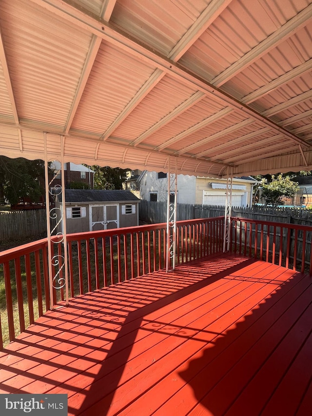 wooden terrace with fence, a storage unit, a carport, and an outbuilding