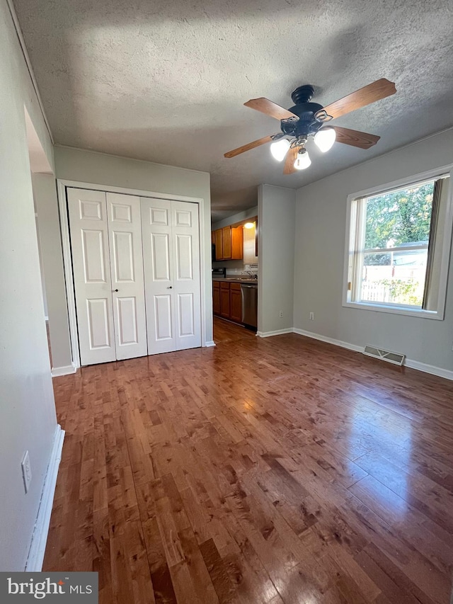 unfurnished bedroom featuring visible vents, a textured ceiling, baseboards, and wood finished floors