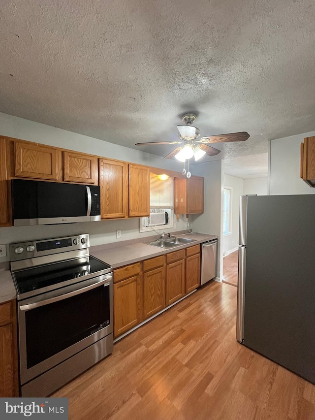 kitchen featuring light wood-style flooring, appliances with stainless steel finishes, brown cabinets, light countertops, and a sink