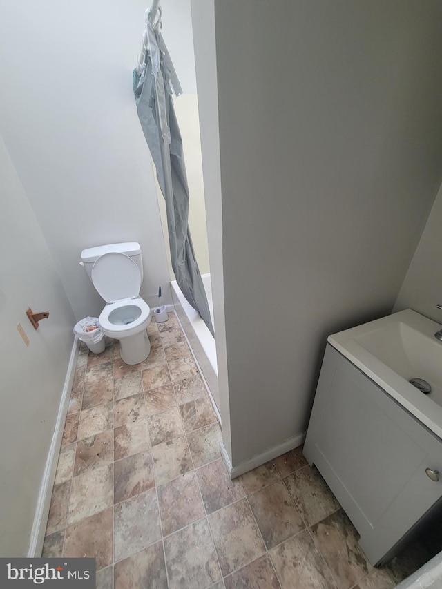 bathroom featuring toilet, vanity, baseboards, a shower with curtain, and stone finish floor