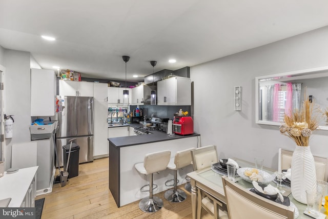 kitchen featuring light hardwood / wood-style flooring, pendant lighting, stainless steel refrigerator, kitchen peninsula, and stove