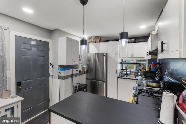 kitchen featuring wall chimney range hood, hanging light fixtures, white cabinets, stainless steel refrigerator, and sink