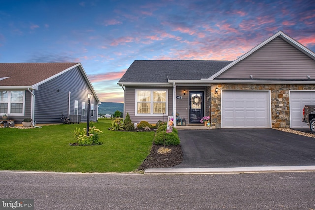 view of front facade featuring a shingled roof, stone siding, aphalt driveway, an attached garage, and a yard