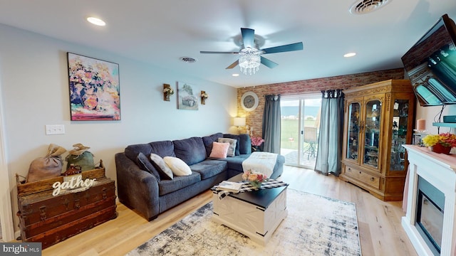 living area with a glass covered fireplace, visible vents, ceiling fan, and light wood finished floors