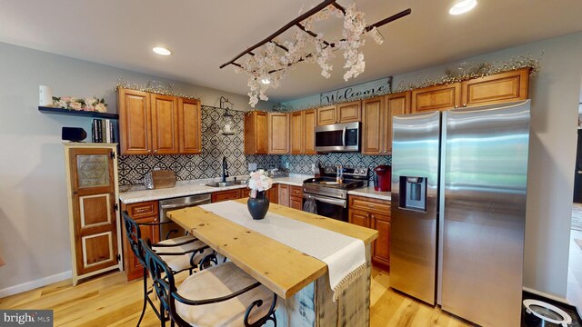 kitchen featuring appliances with stainless steel finishes, sink, tasteful backsplash, and light hardwood / wood-style flooring