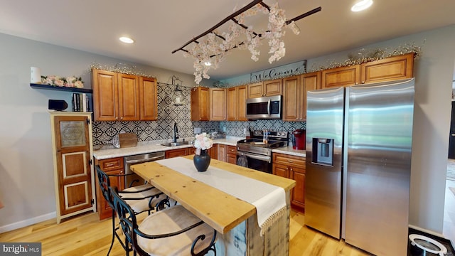 kitchen featuring brown cabinets, stainless steel appliances, light countertops, a sink, and light wood-type flooring