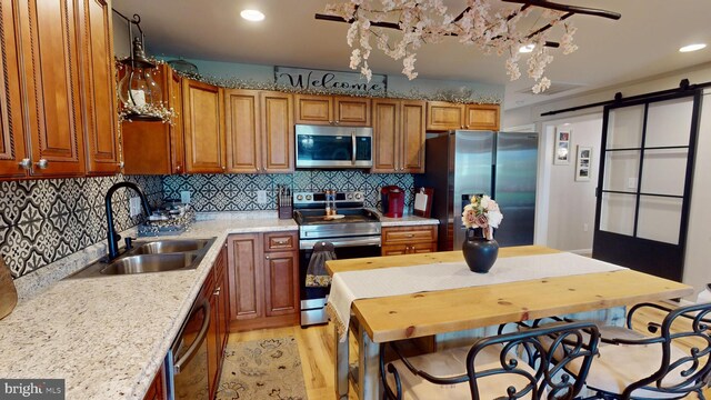 kitchen with decorative backsplash, a barn door, light hardwood / wood-style floors, sink, and stainless steel appliances