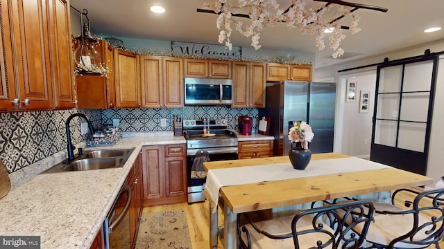 kitchen featuring appliances with stainless steel finishes, brown cabinetry, a sink, and light stone countertops