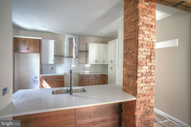 kitchen with sink, white cabinets, kitchen peninsula, wall chimney exhaust hood, and decorative backsplash