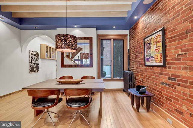 dining room with brick wall, beam ceiling, and light hardwood / wood-style floors