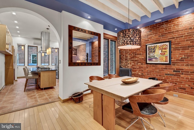 dining area featuring light wood-type flooring, beamed ceiling, and brick wall