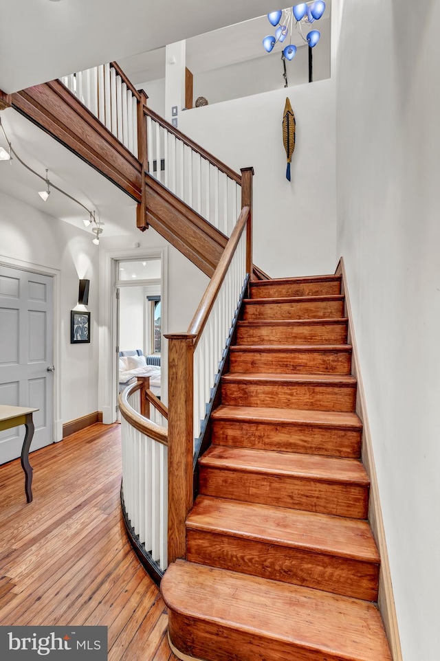 stairs featuring a towering ceiling, hardwood / wood-style floors, and a notable chandelier