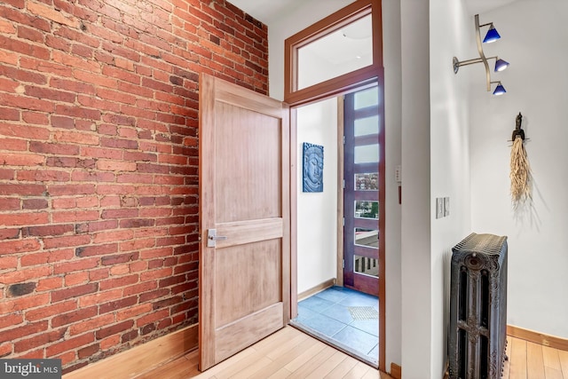 foyer with radiator, light hardwood / wood-style flooring, and brick wall