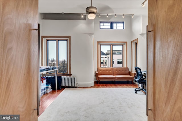 living area with ceiling fan, radiator heating unit, hardwood / wood-style flooring, and a high ceiling